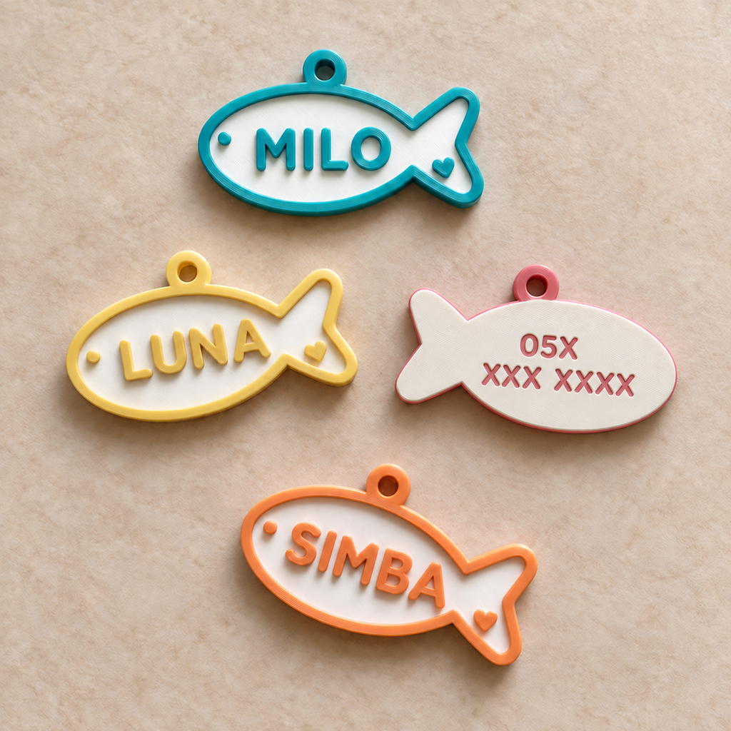 Fish-shaped cat ID tags showing English names on the front and a Saudi 05 phone-number placeholder on the back